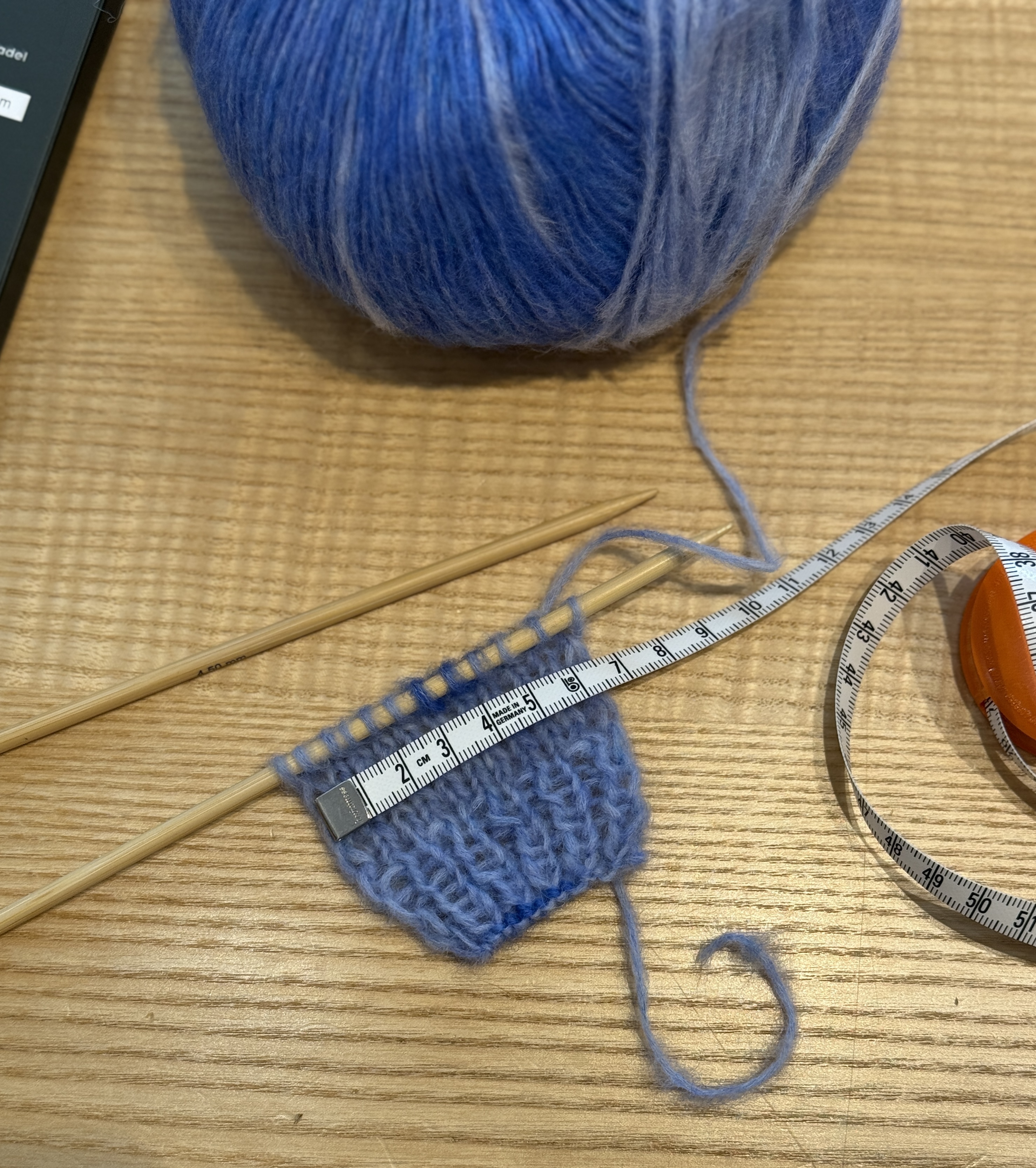 Ein kleines gestricktes Probequadrat mit Maßband daneben